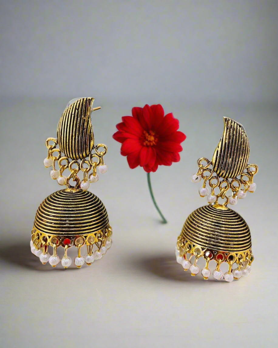 Gold and pearl earrings on a stand with a floral background