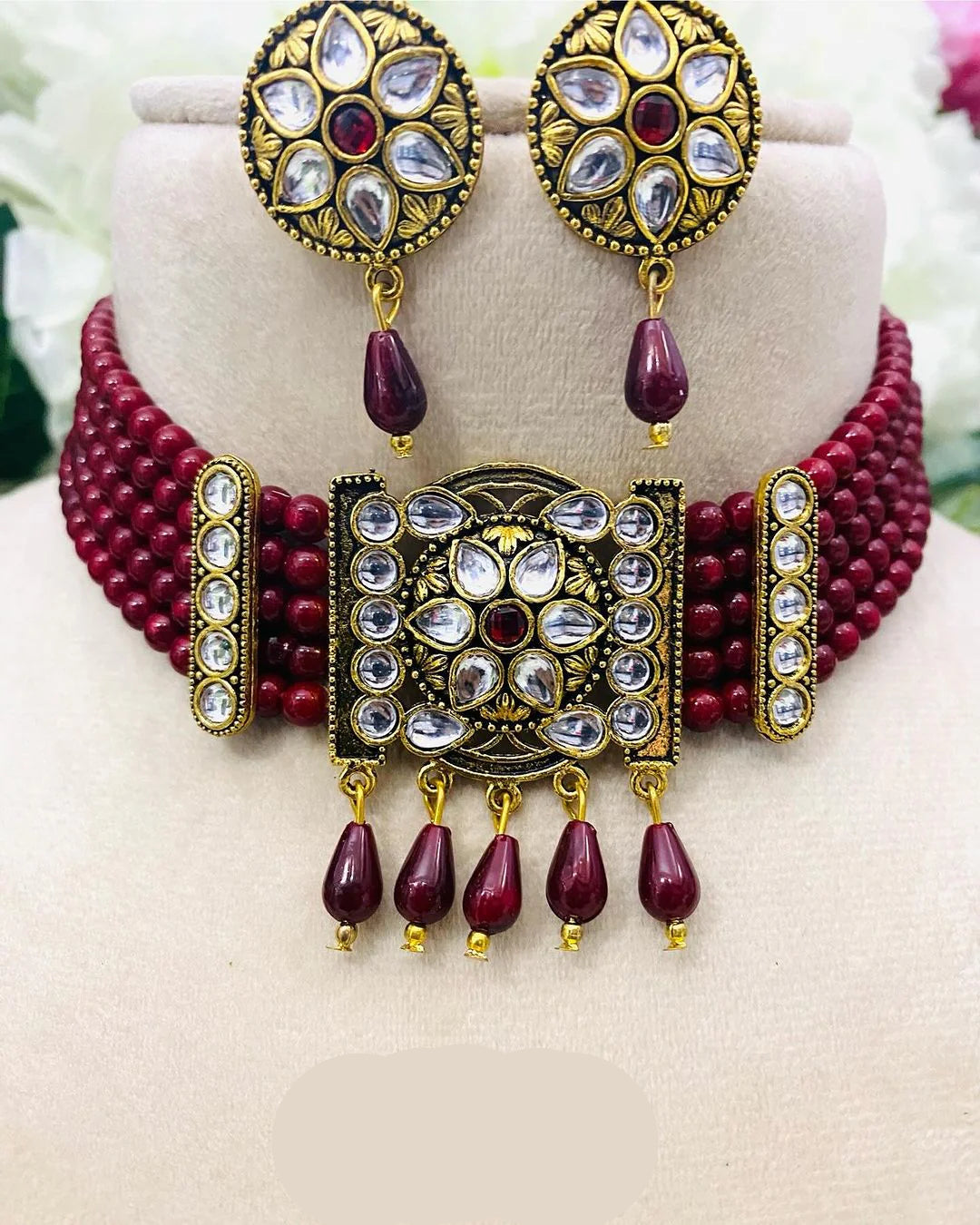Ornate jewelry set with maroon beads and gold accents on a mannequin.