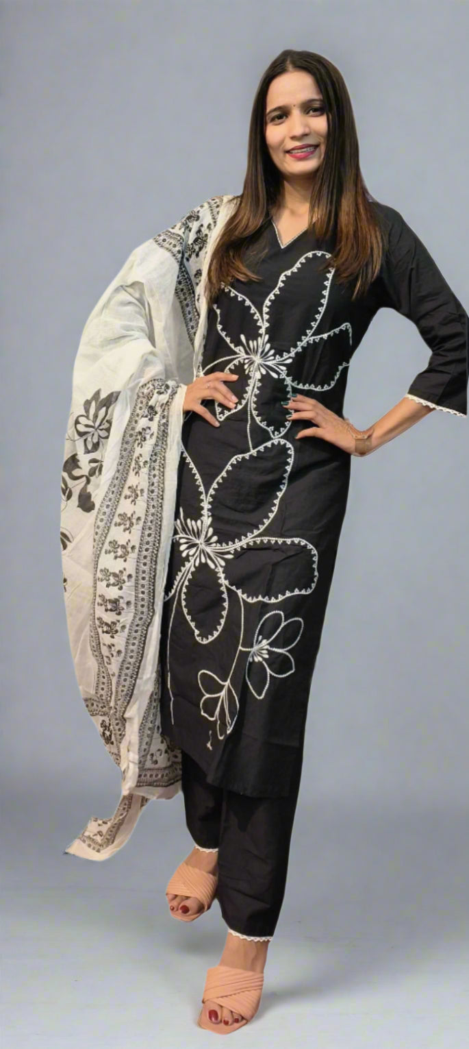 Woman wearing a black outfit with white floral embroidery and a matching shawl on a gray background